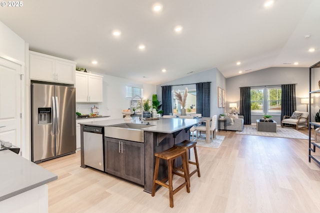 kitchen featuring stainless steel appliances, a sink, white cabinetry, open floor plan, and vaulted ceiling