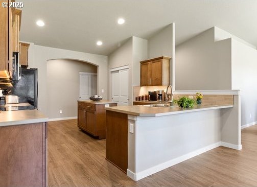 51013 Mckenzie Hwy, Vida, OR 97488 - kitchen featuring arched walkways, a sink, light wood finished floors, brown cabinetry, and baseboards