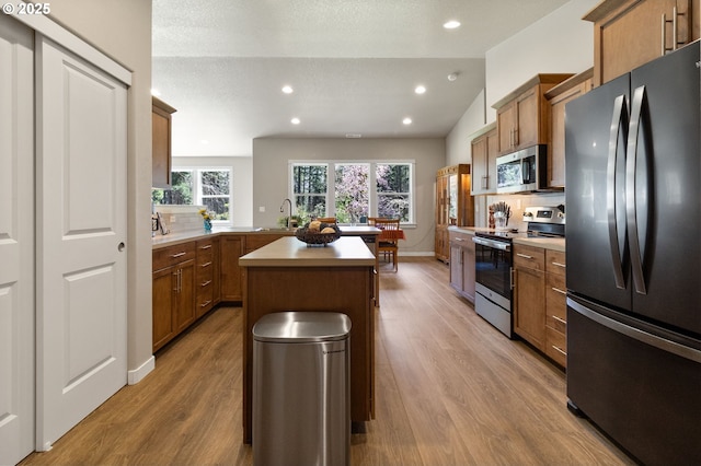 kitchen with a sink, brown cabinets, light wood-style floors, stainless steel appliances, and light countertops