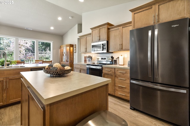 kitchen with a center island, a sink, light wood-type flooring, vaulted ceiling, and appliances with stainless steel finishes