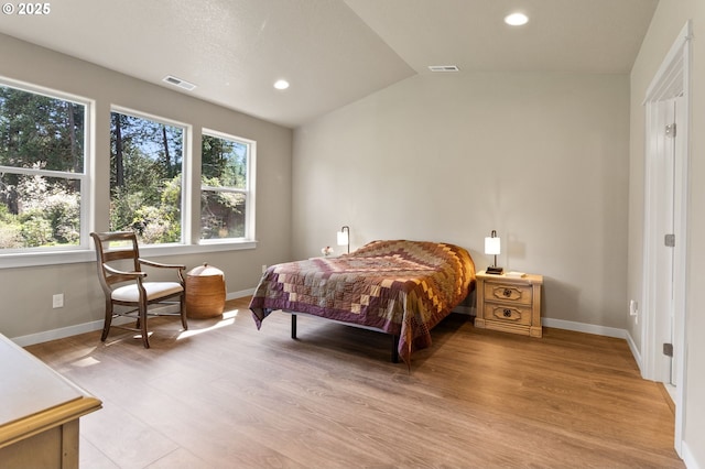 bedroom featuring light wood-style floors, vaulted ceiling, visible vents, and baseboards