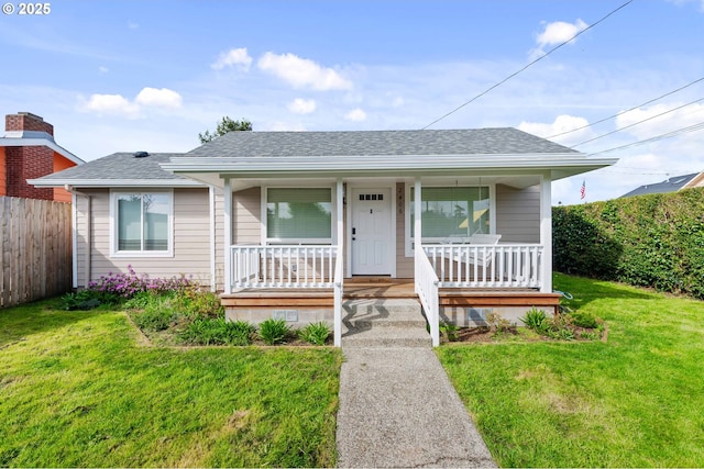 view of front facade featuring roof with shingles, covered porch, a front lawn, and fence