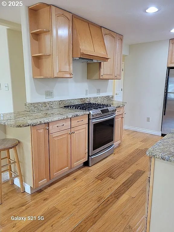 2525 Pine St, Seaside, OR 97138 - kitchen featuring appliances with stainless steel finishes, premium range hood, light wood finished floors, light stone counters, and light brown cabinets