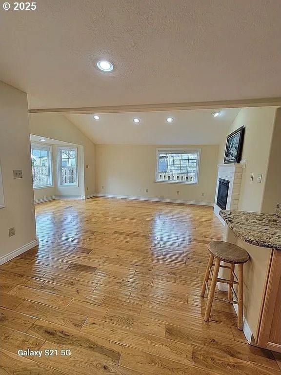 2525 Pine St, Seaside, OR 97138 - unfurnished living room featuring light wood finished floors, baseboards, a glass covered fireplace, a textured ceiling, and recessed lighting