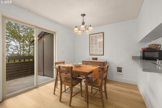 dining space featuring baseboards, a notable chandelier, light wood-style flooring, and a textured ceiling