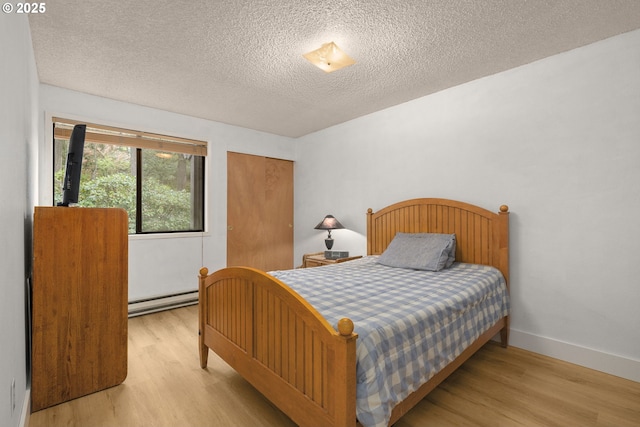 bedroom featuring a textured ceiling, a closet, baseboard heating, and wood finished floors