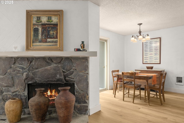 dining room featuring heating unit, light wood-style flooring, baseboards, a stone fireplace, and a chandelier