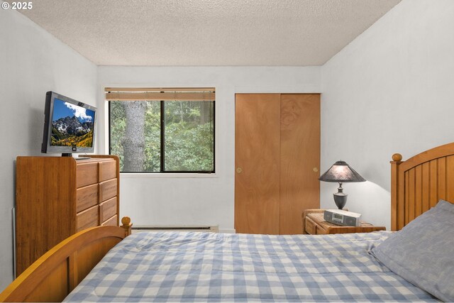 bedroom with a textured ceiling, a closet, and baseboard heating