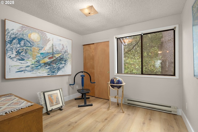 exercise room with a textured ceiling, wood finished floors, baseboards, and a baseboard heating unit