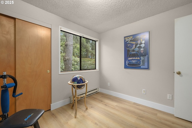 interior space featuring a baseboard heating unit, light wood-style floors, a textured ceiling, and baseboards