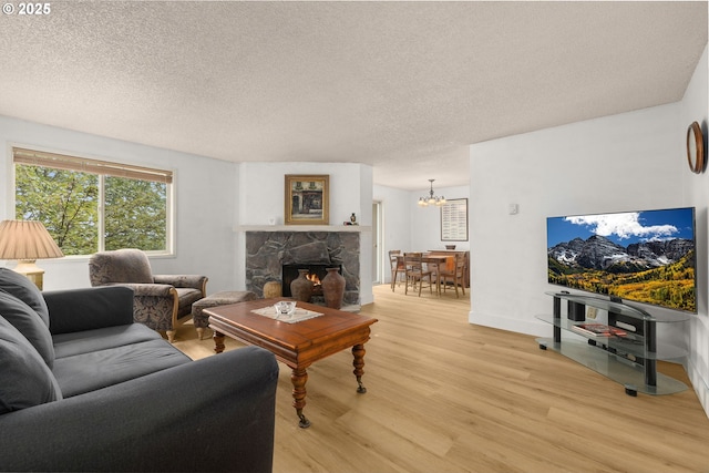 living room with a notable chandelier, a fireplace, light wood-style flooring, and a textured ceiling