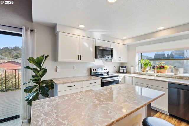 kitchen featuring white cabinets, light stone countertops, appliances with stainless steel finishes, and a sink