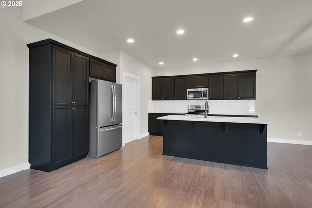 kitchen featuring a breakfast bar area, wood finished floors, stainless steel appliances, light countertops, and backsplash