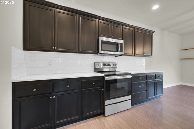 kitchen with baseboards, light wood-style flooring, appliances with stainless steel finishes, light countertops, and backsplash