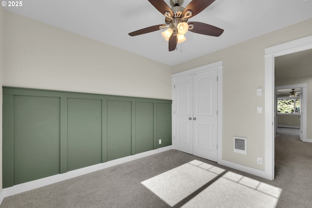 unfurnished bedroom featuring a decorative wall, carpet flooring, a ceiling fan, visible vents, and a closet