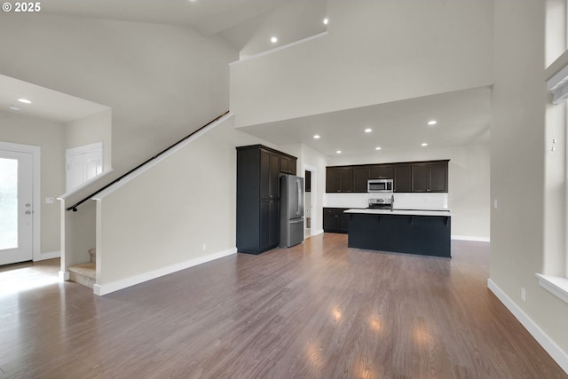 kitchen with high vaulted ceiling, stainless steel appliances, wood finished floors, open floor plan, and a center island