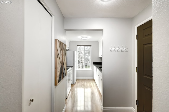 kitchen with refrigerator, white cabinetry, light hardwood / wood-style floors, a textured ceiling, and electric stove