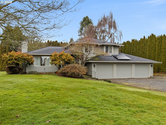 view of front of house with an attached garage, driveway, a front lawn, and solar panels