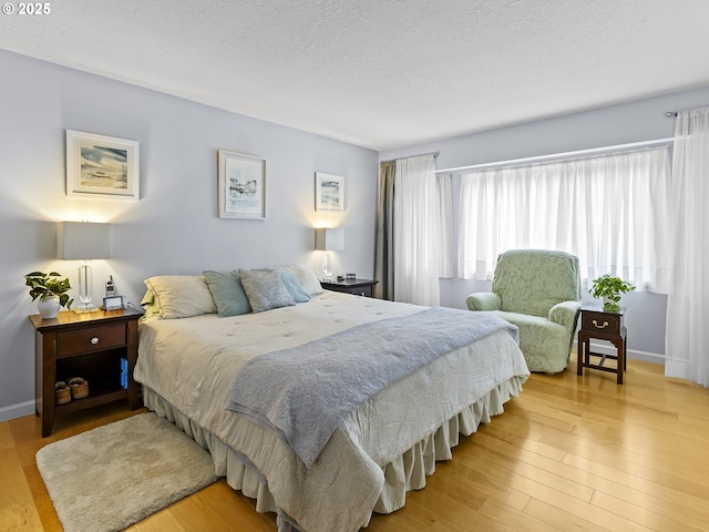 bedroom with light wood finished floors, baseboards, and a textured ceiling