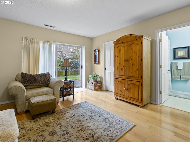 living area featuring baseboards, visible vents, light wood-style flooring, and a textured ceiling