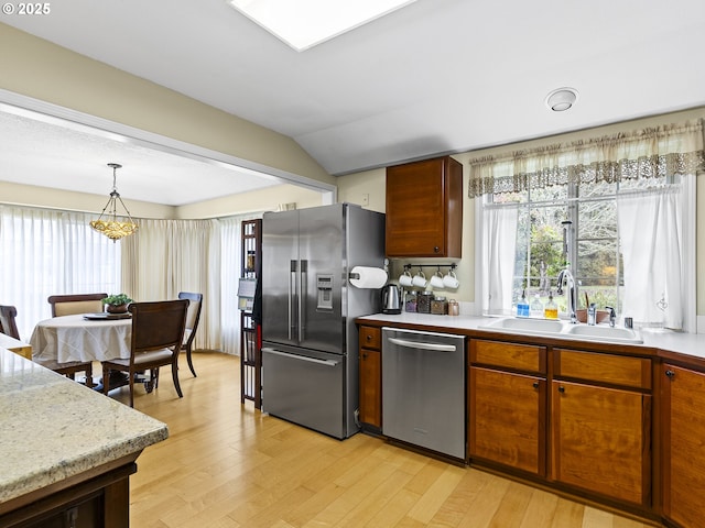 kitchen with stainless steel appliances, a sink, hanging light fixtures, light countertops, and light wood-type flooring