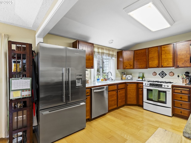 kitchen with appliances with stainless steel finishes, light countertops, a sink, and light wood-style flooring