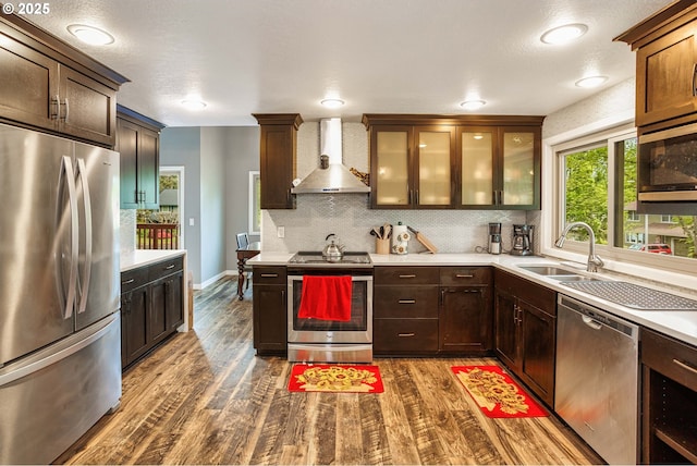 kitchen featuring stainless steel appliances, wall chimney exhaust hood, a sink, dark wood-style floors, and decorative backsplash