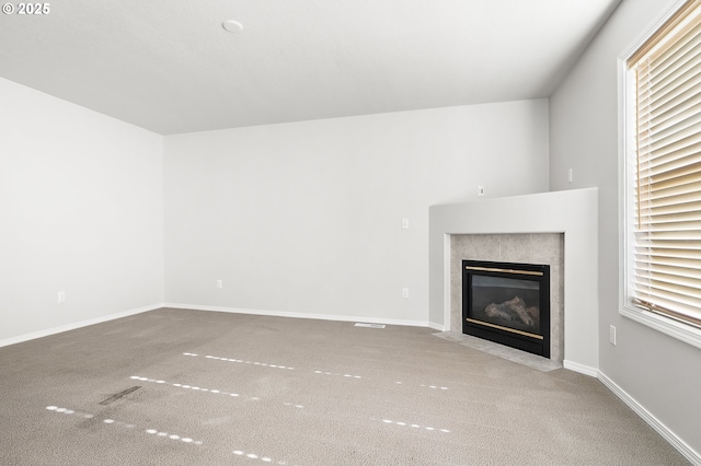 unfurnished living room featuring carpet flooring, a tiled fireplace, and baseboards