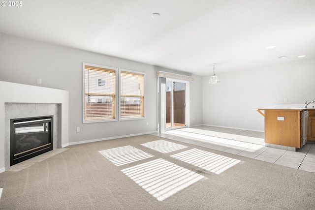 unfurnished living room with light tile patterned floors, baseboards, a tile fireplace, light colored carpet, and a sink