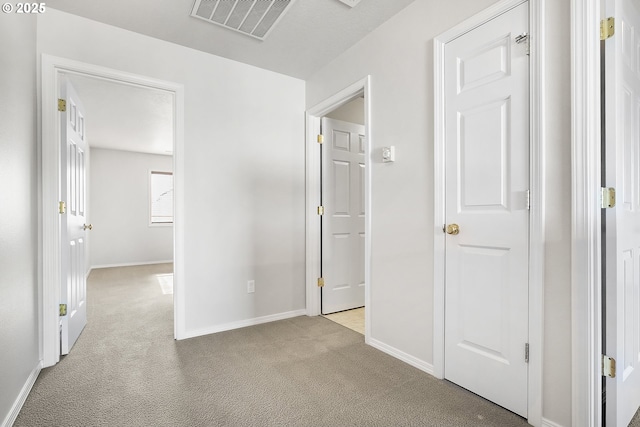 hall with visible vents, light carpet, and baseboards