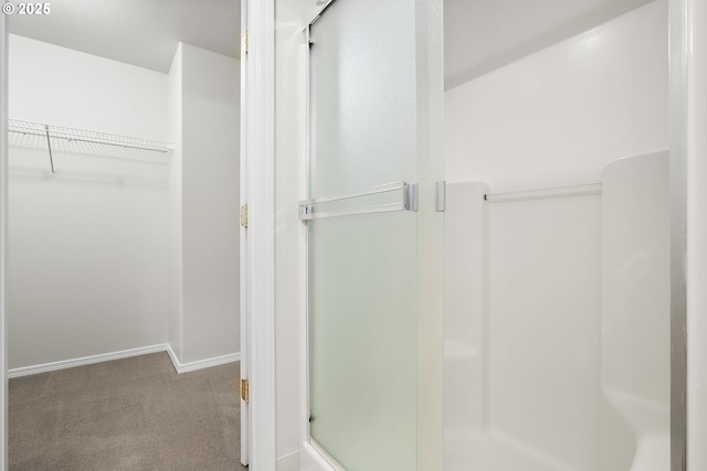 full bathroom with a walk in closet, a shower with door, and baseboards