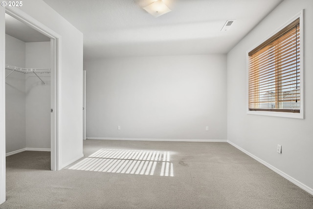 unfurnished bedroom with a walk in closet, a closet, visible vents, light carpet, and baseboards