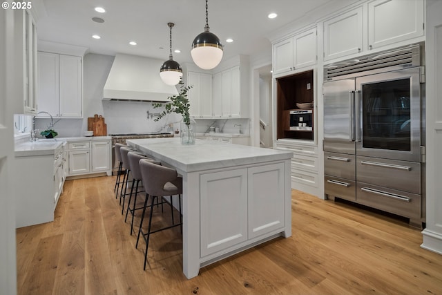 kitchen featuring white cabinetry, a center island, hanging light fixtures, and custom range hood