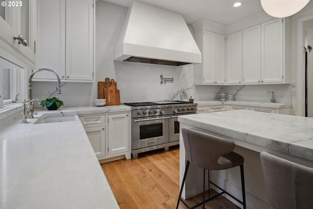 kitchen featuring white cabinetry, sink, double oven range, custom range hood, and light hardwood / wood-style flooring