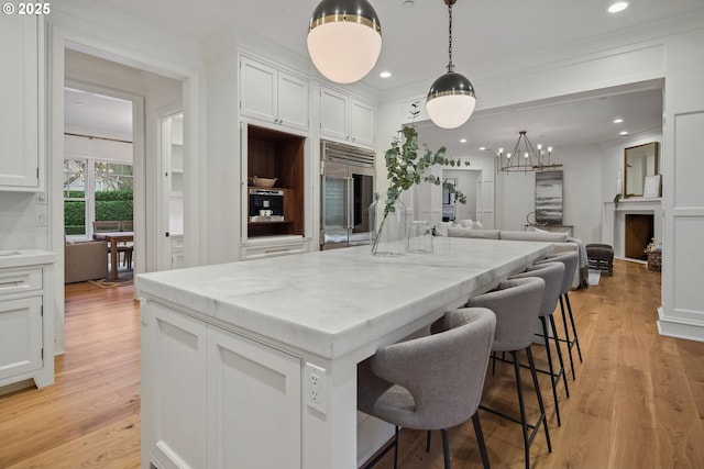 kitchen with a kitchen island, light hardwood / wood-style floors, white cabinets, a kitchen bar, and stainless steel built in fridge