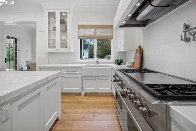 kitchen with sink, light hardwood / wood-style flooring, white cabinetry, light stone countertops, and range with two ovens