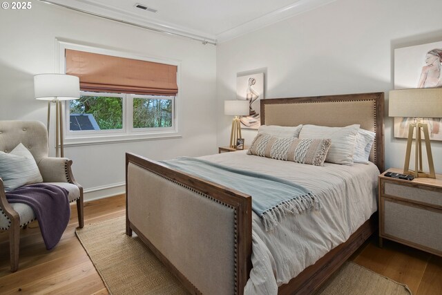 bedroom with visible vents, crown molding, and wood finished floors