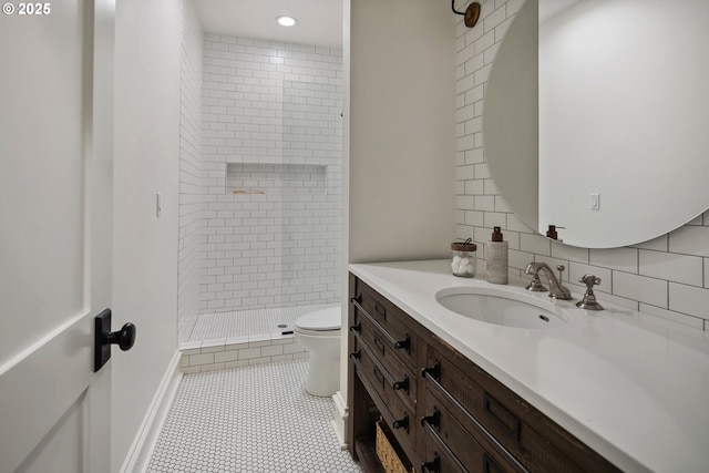 bathroom featuring vanity, tiled shower, backsplash, and toilet