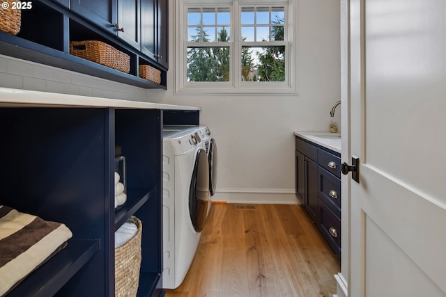 laundry area with cabinets, separate washer and dryer, sink, and light hardwood / wood-style flooring