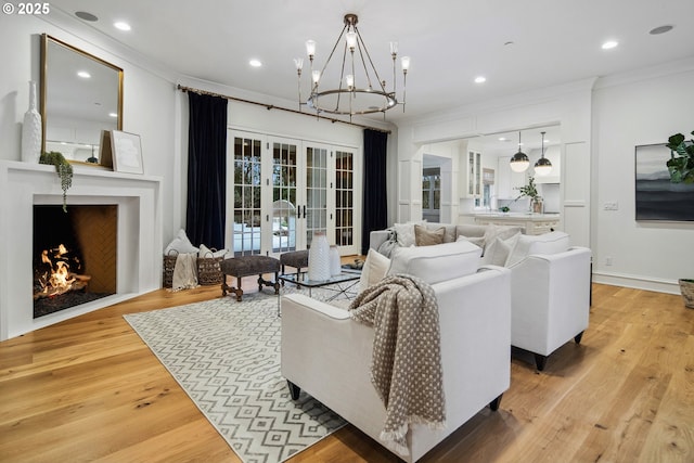 living room featuring french doors, crown molding, an inviting chandelier, light hardwood / wood-style flooring, and a fireplace