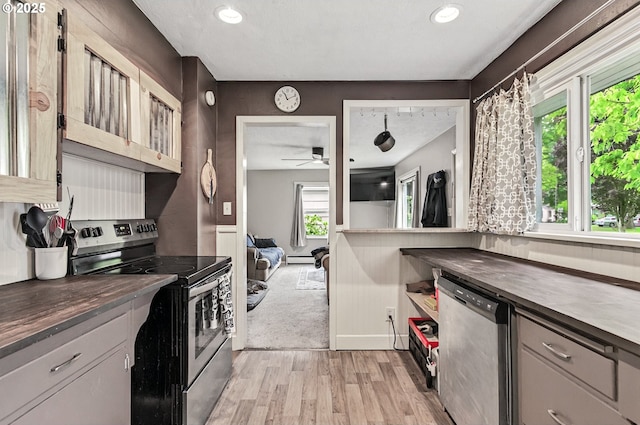 kitchen featuring appliances with stainless steel finishes, light wood-type flooring, dark countertops, baseboard heating, and ceiling fan