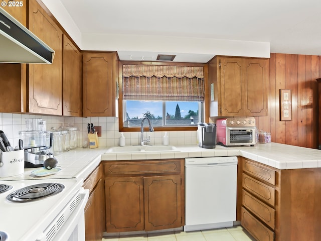 kitchen featuring tasteful backsplash, brown cabinetry, a sink, ventilation hood, and white appliances