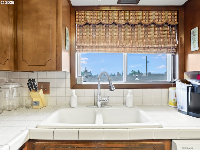 kitchen featuring tile countertops, backsplash, brown cabinetry, and a sink