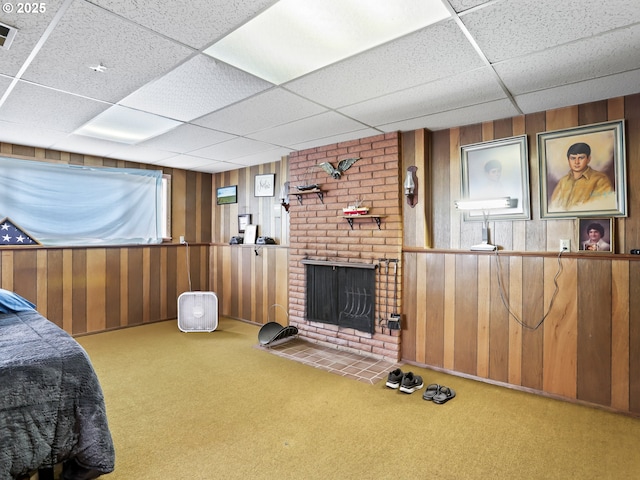 carpeted bedroom with a paneled ceiling, wooden walls, a fireplace, and visible vents