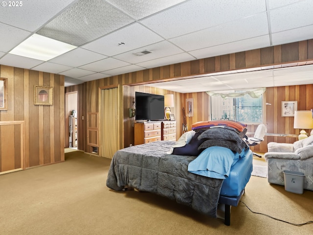 carpeted bedroom featuring a paneled ceiling, visible vents, and wooden walls