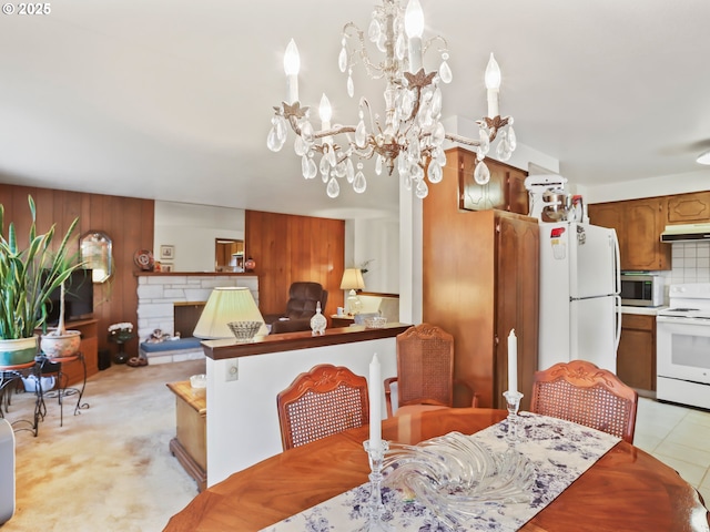 dining room featuring wood walls, a stone fireplace, and an inviting chandelier