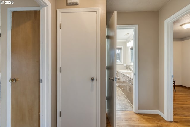 corridor with light wood-type flooring, a textured ceiling, and ornamental molding