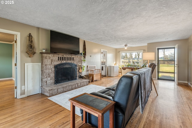 living room featuring ceiling fan, a textured ceiling, light hardwood / wood-style floors, and a fireplace