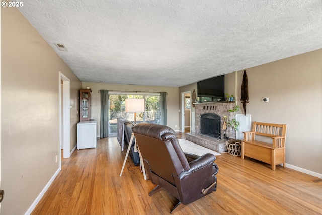 living room featuring a brick fireplace, light hardwood / wood-style flooring, and a textured ceiling