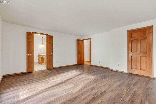 unfurnished bedroom with ensuite bathroom and light hardwood / wood-style floors